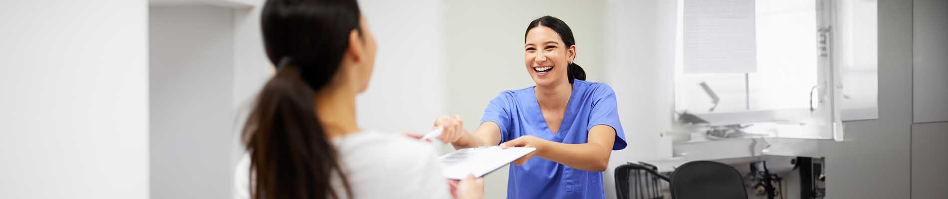 The image shows two individuals in a professional setting one appears to be handing over an item to another who seems to be receiving it, possibly in a healthcare or service environment.