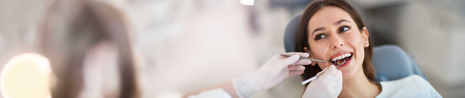 A woman sitting at a dental chair with a dentist performing a procedure on her teeth, using a drill.