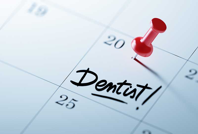 The image shows a calendar with a red pin marking a specific date on which the word  dentist  is written, suggesting an appointment scheduled for dental care.