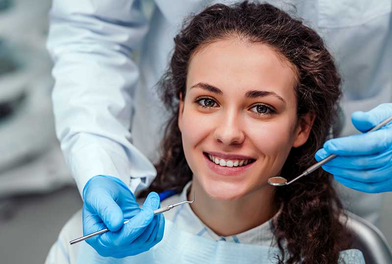A woman receiving dental care from a professional, with both smiling at the camera.
