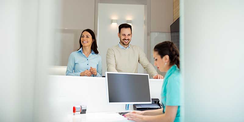 The image depicts a modern office reception area with a sleek, contemporary design featuring a wooden desk and a white countertop.